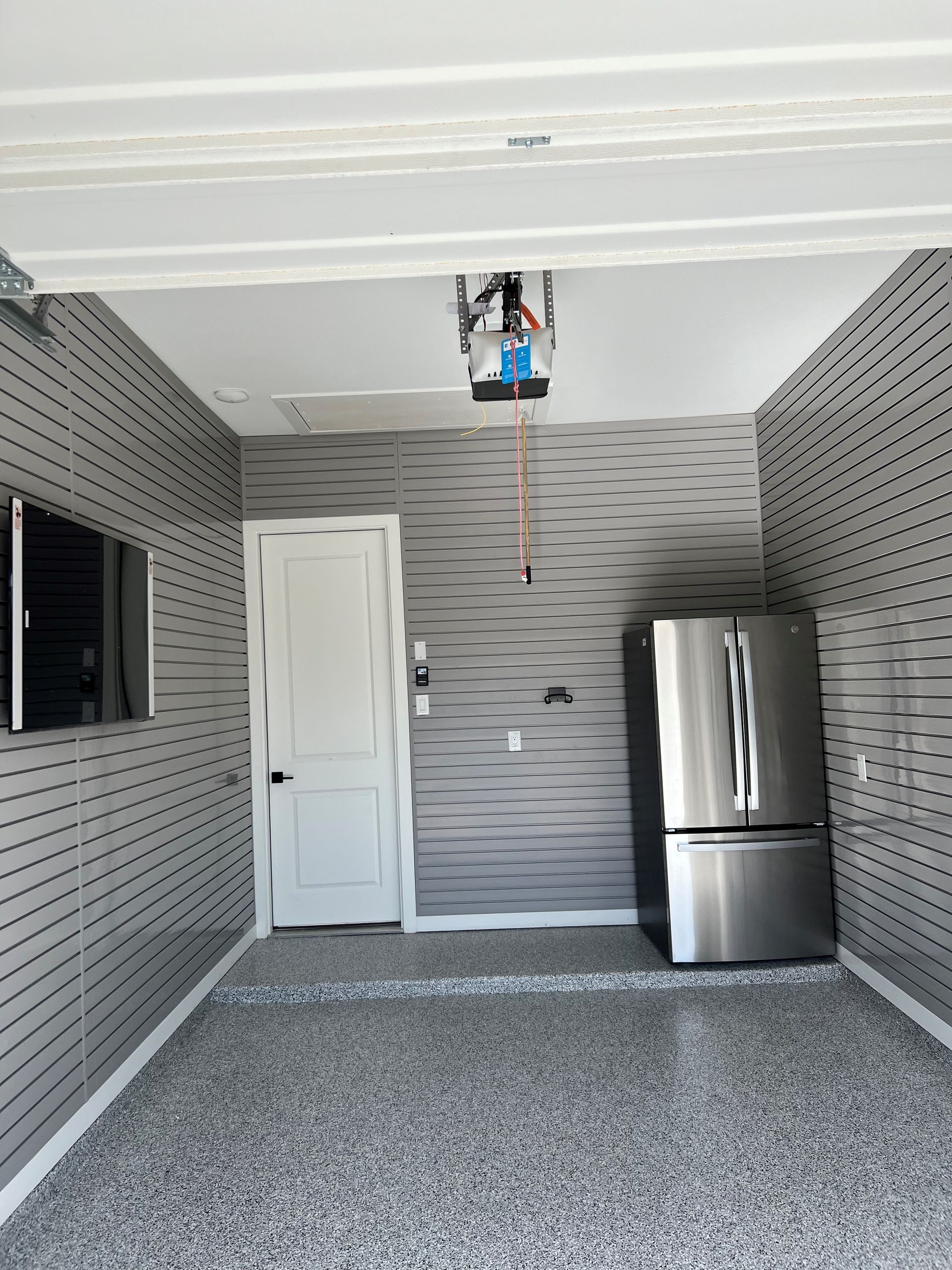 A garage with a stainless steel refrigerator and a ceiling lift.