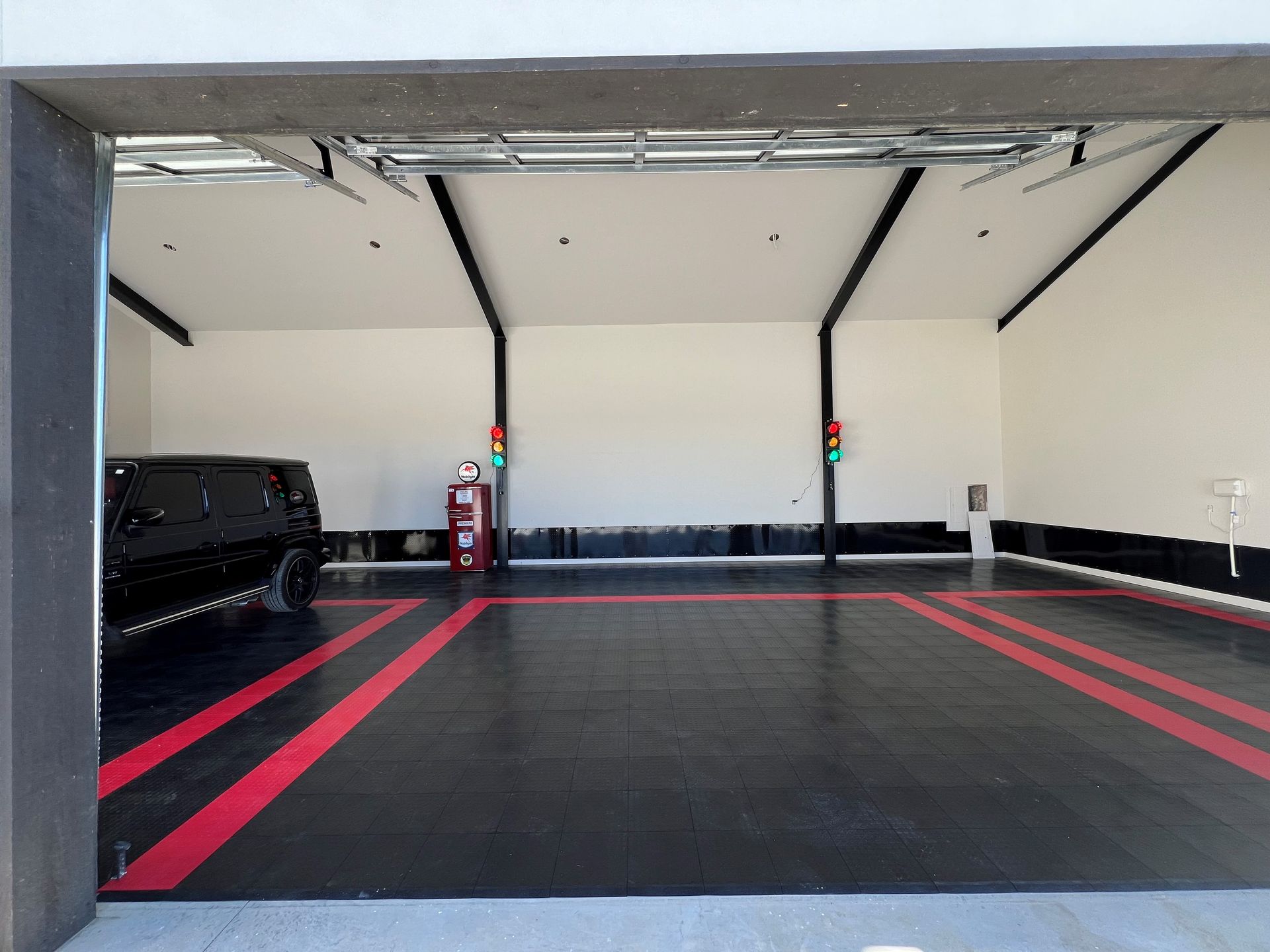 A black car is parked in a garage with red stripes on the floor.