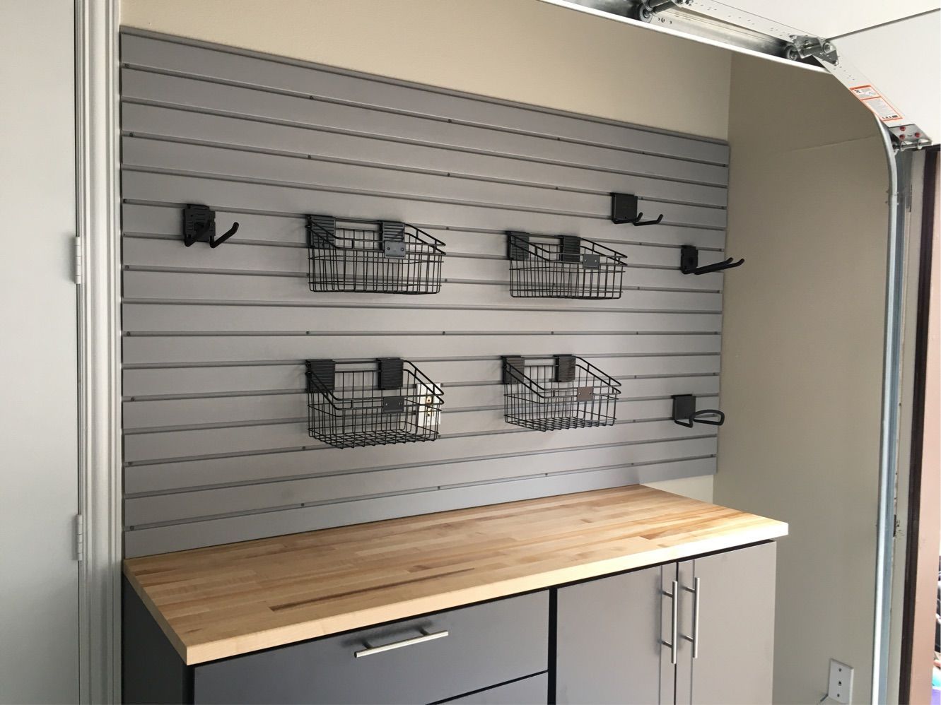 A garage with a wooden counter top and a slat wall with baskets on it.