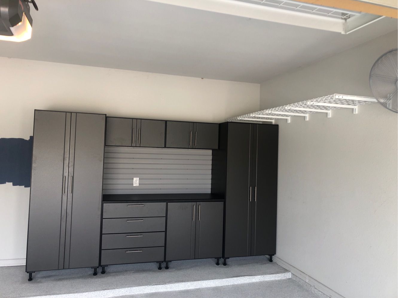 A garage with a lot of cabinets and drawers and a fan on the wall.