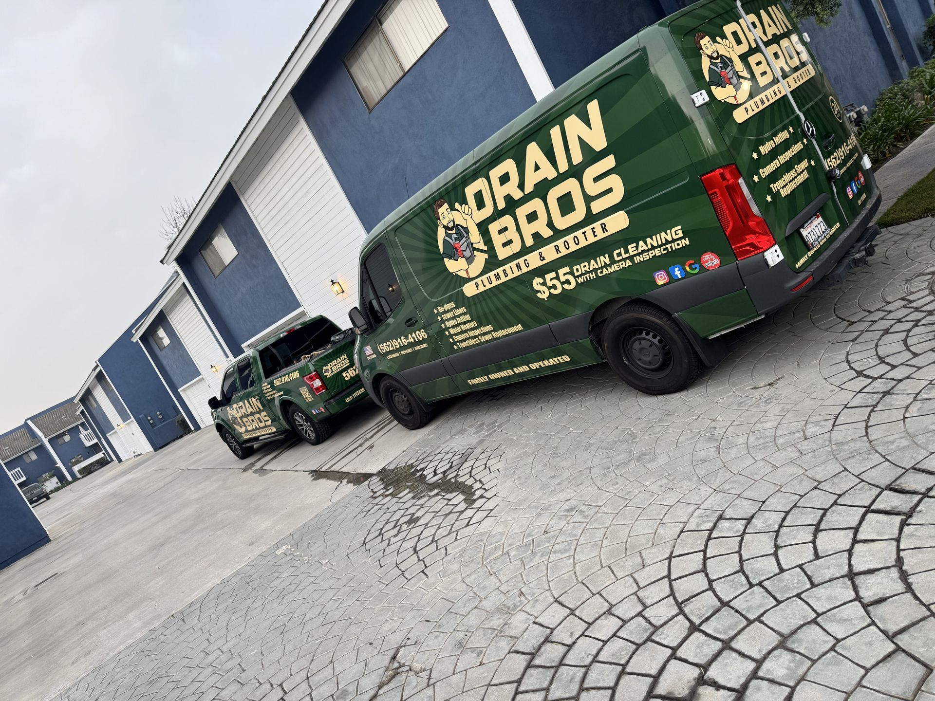 Green and black Drain Bros van and truck parked in front of a blue apartment building