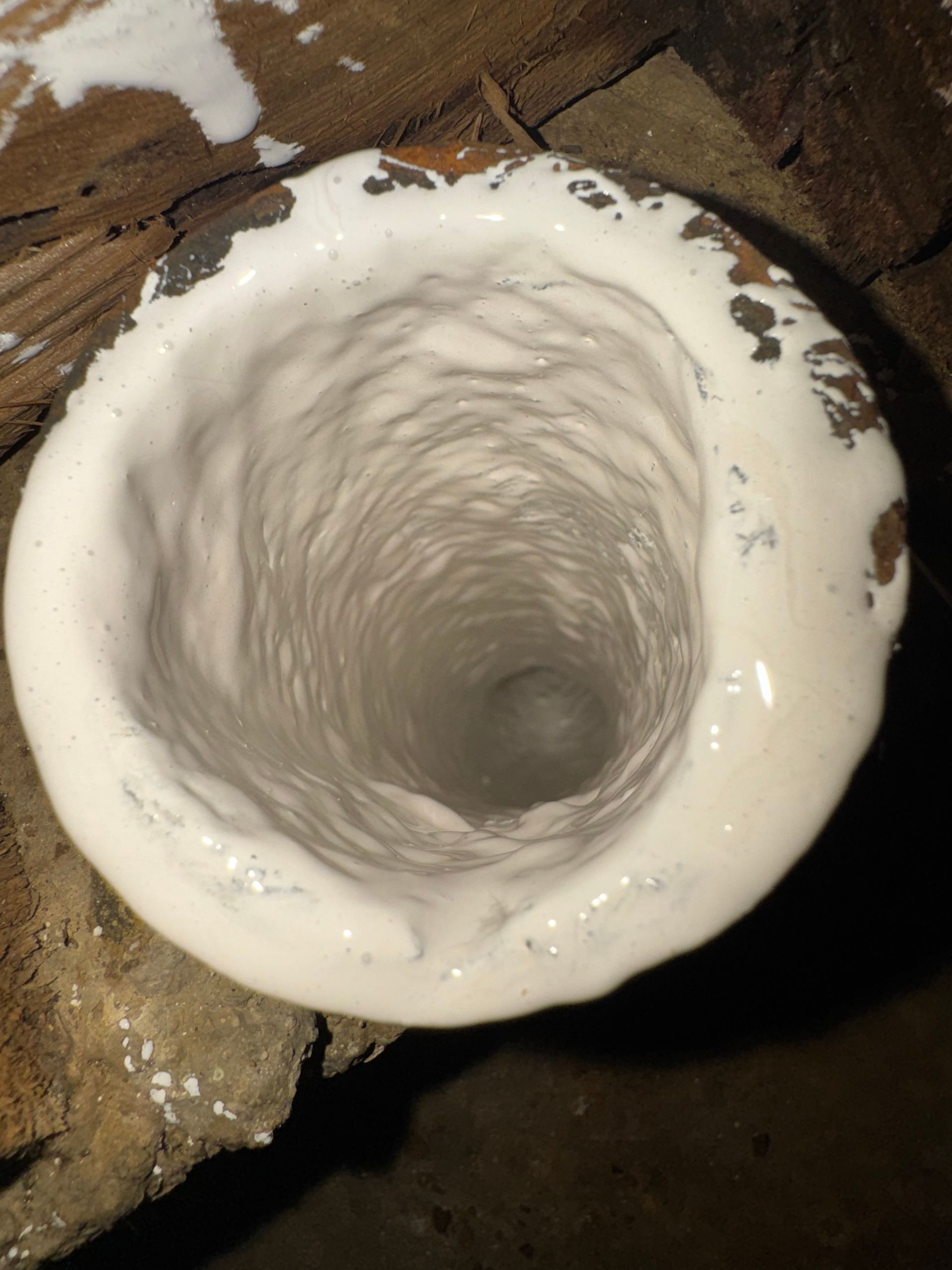 Top-down view of a white-coated ceramic crucible with a swirling interior, set on a dark wood surface.