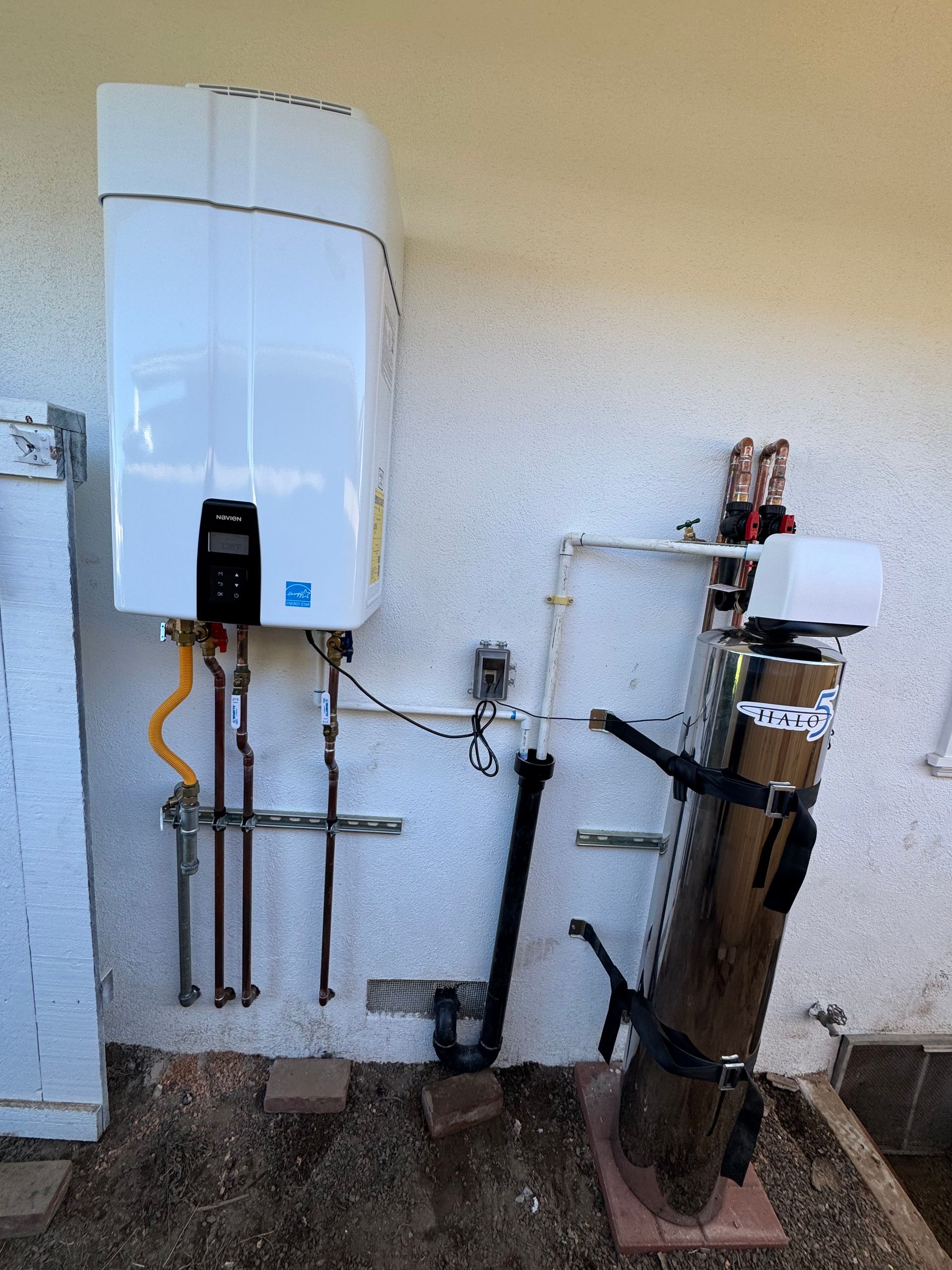 A white tankless water heater and water filtration system mounted on a stucco wall outdoors.