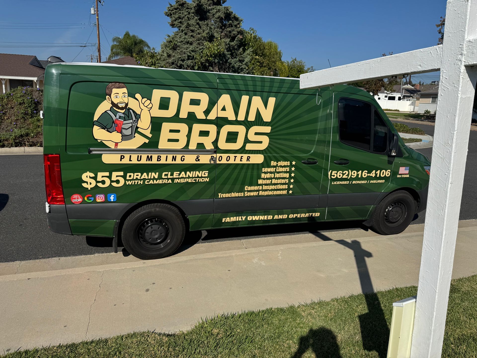 Green Drain Bros. plumbing van parked on a curb. The van has business logos and contact information.