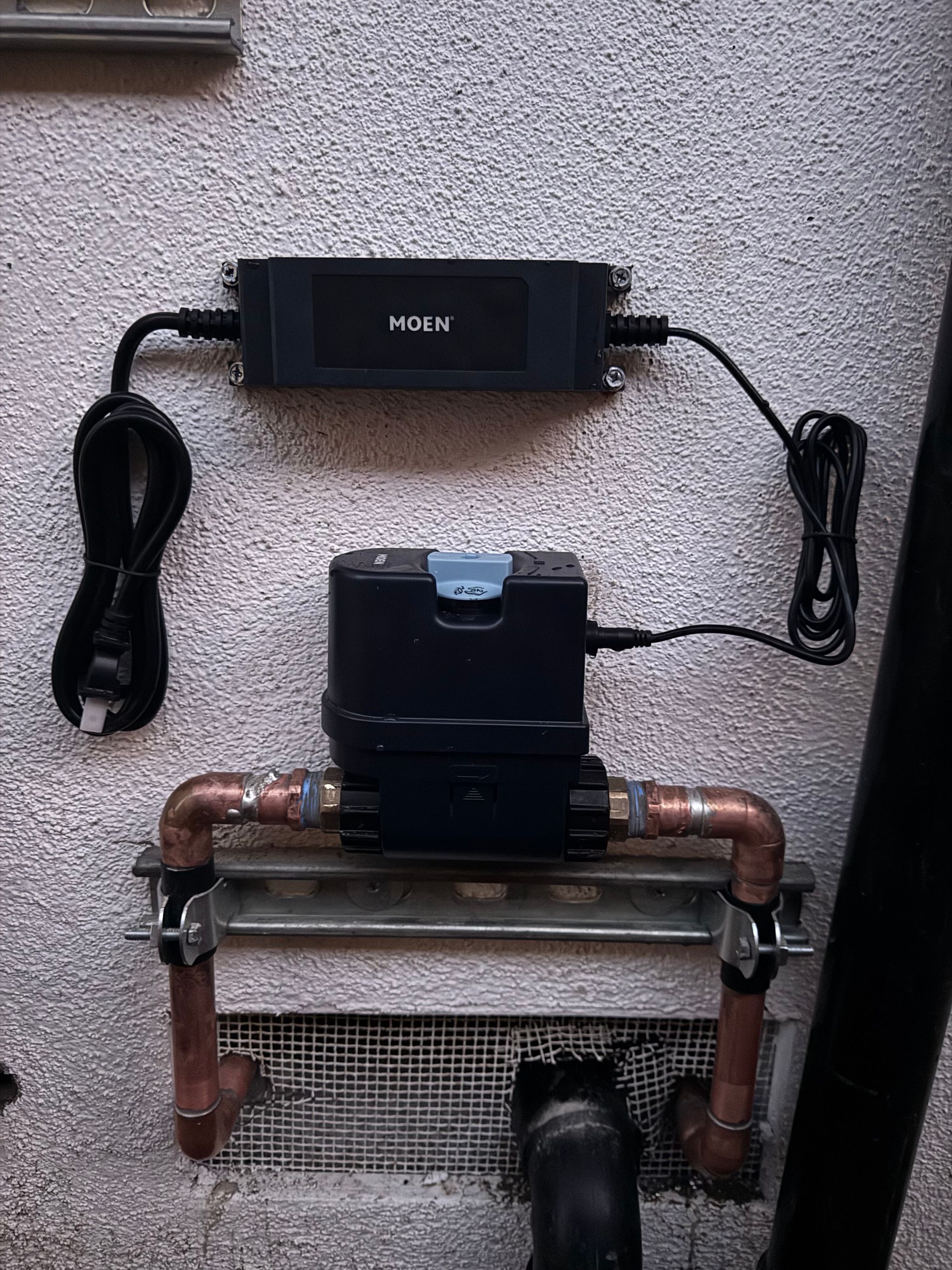 Water meter and related electronics mounted on a textured wall. Copper pipes and black cables are visible.