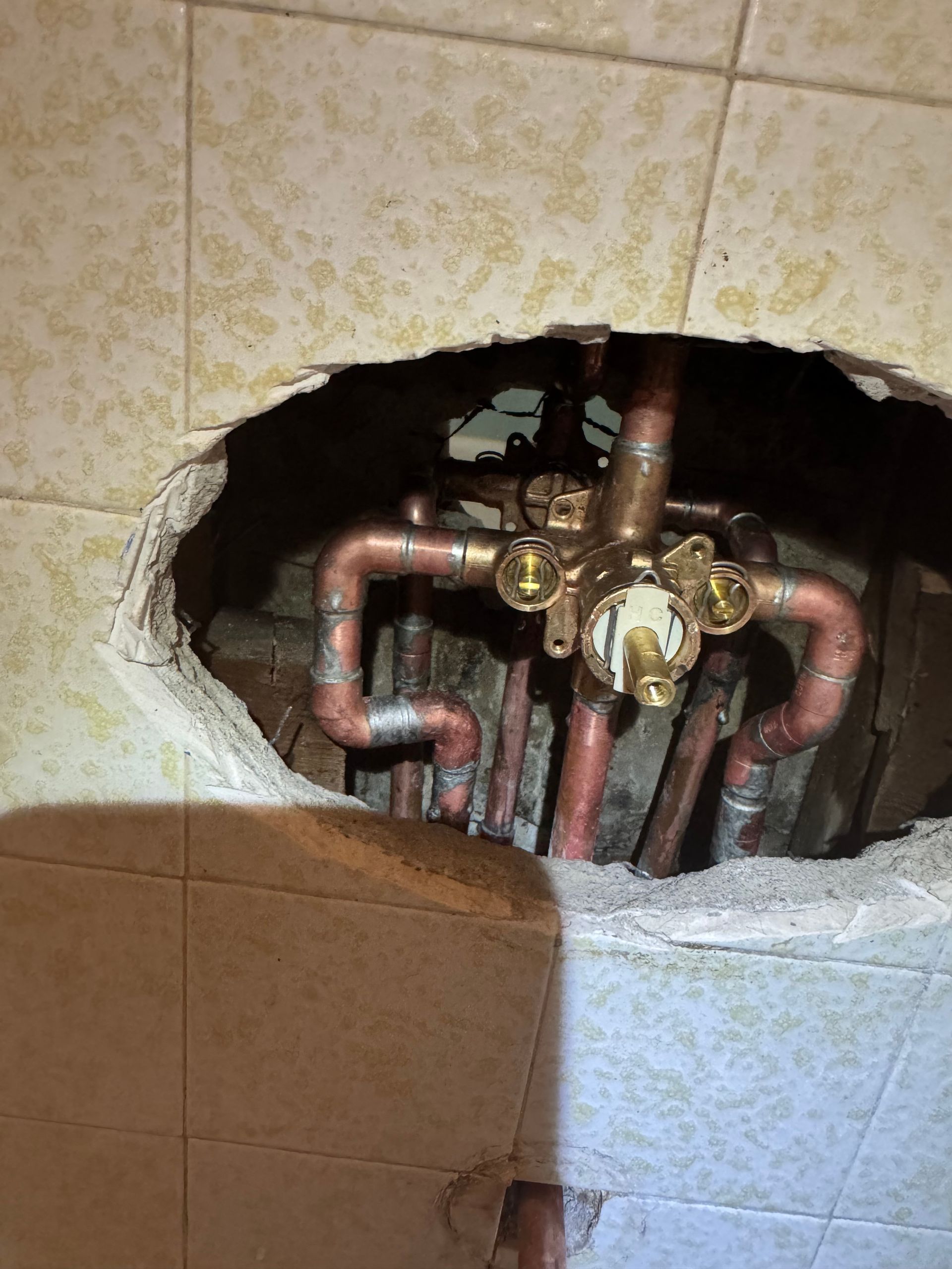 Copper pipes and shower valve exposed in a tiled wall cavity.