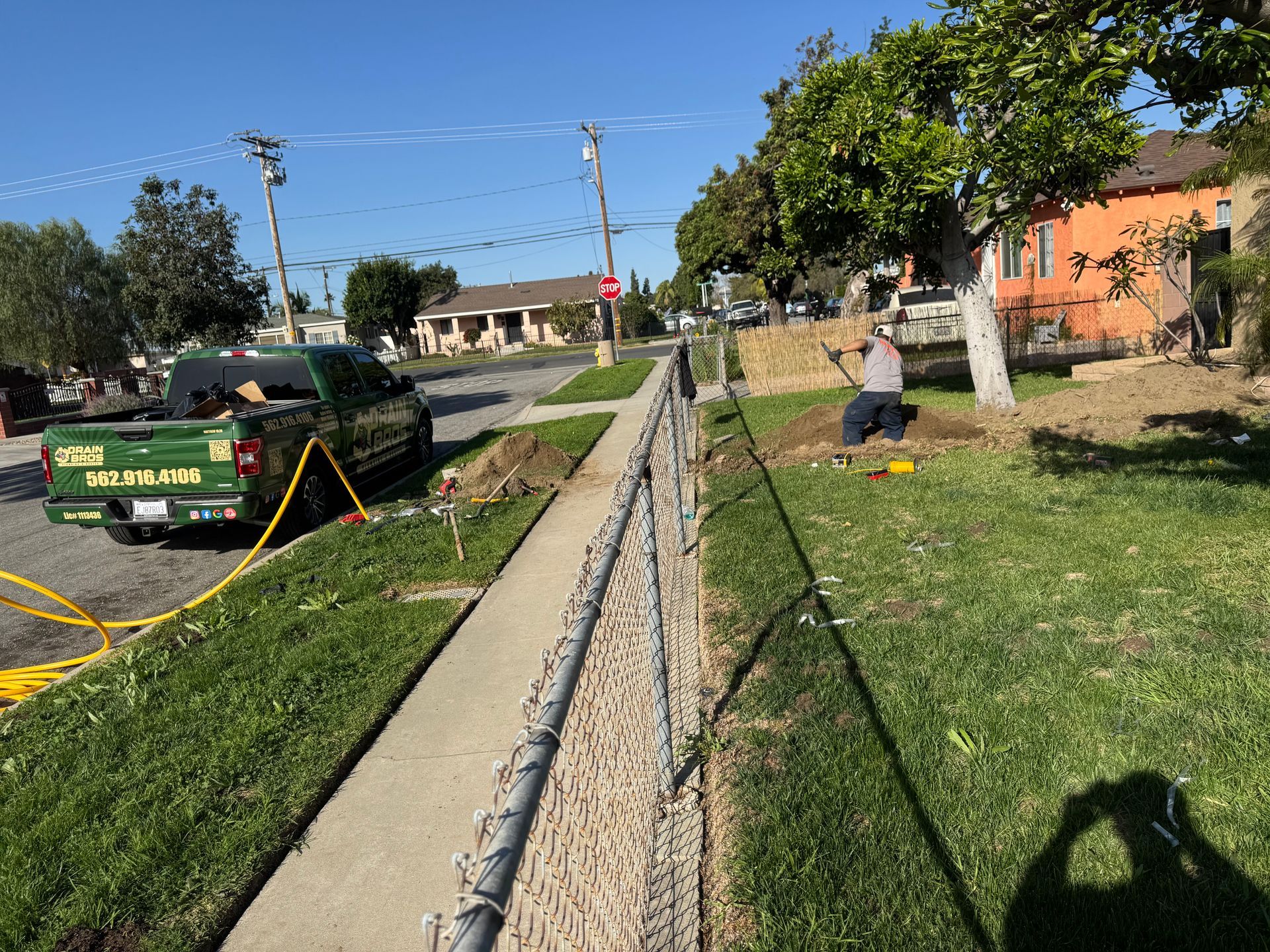 Green truck, man working next to sidewalk, chain link fence, street, residential area.