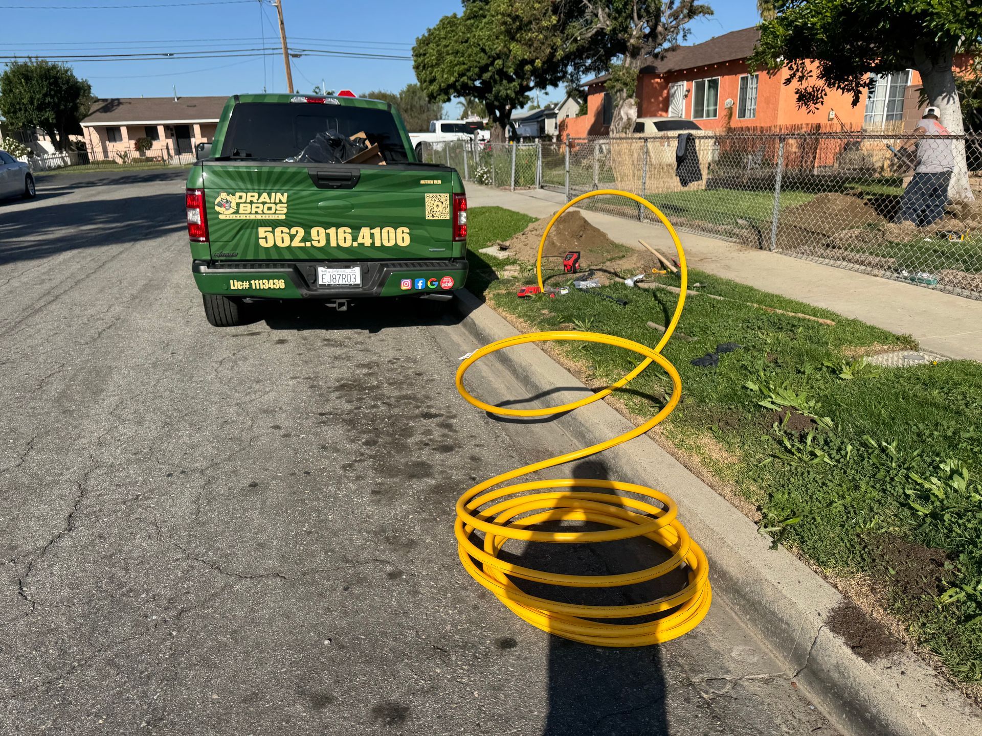Green work truck with yellow coiled hose on a curb next to a residential street.