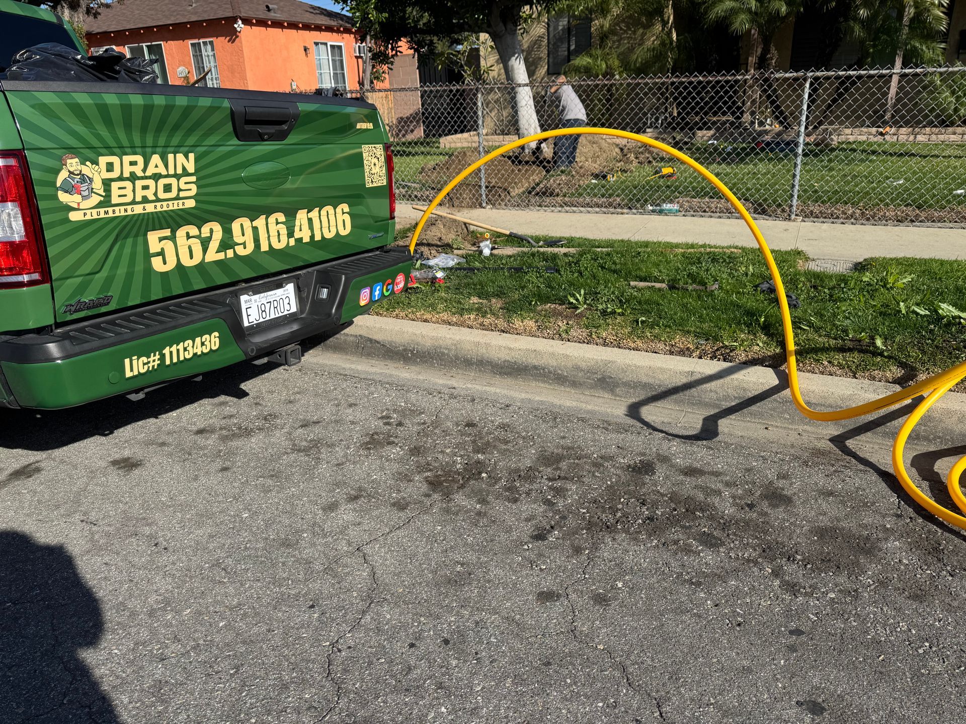 Green Drain Bros truck with a yellow hose extending towards a grassy area beside a road.