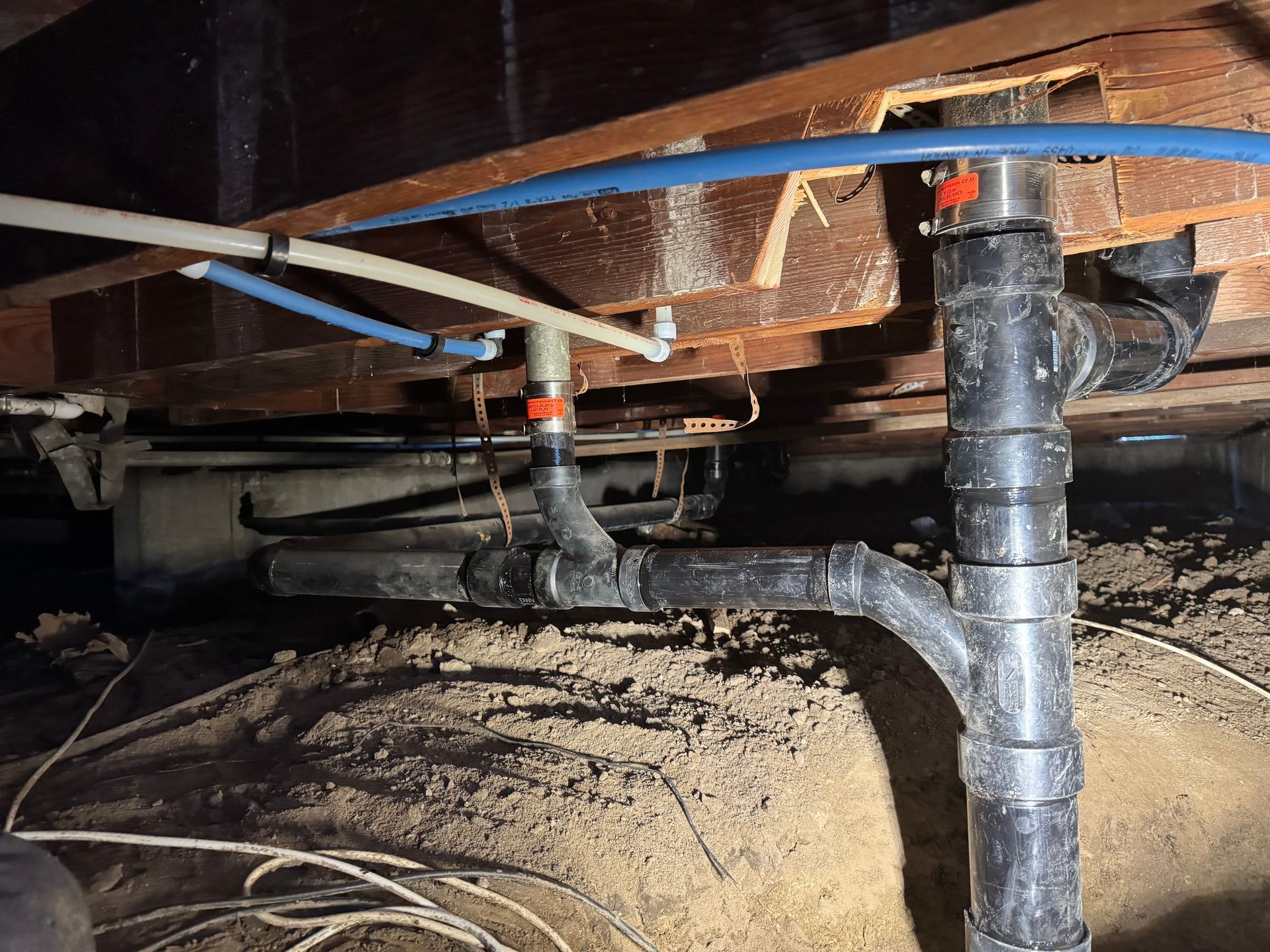 Underneath a wooden structure, plumbing pipes with black and blue tubing are visible.