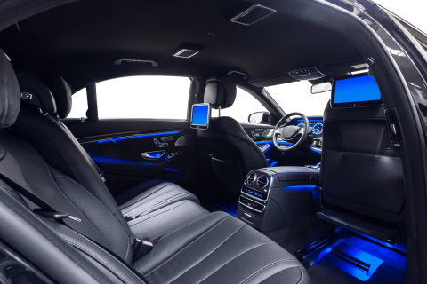 The interior of a luxury sedan featuring black leather seats, rear-seat entertainment screens, and vibrant blue lighting.