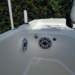 White boat deck with two speakers and a small chrome fitting, near green foliage.