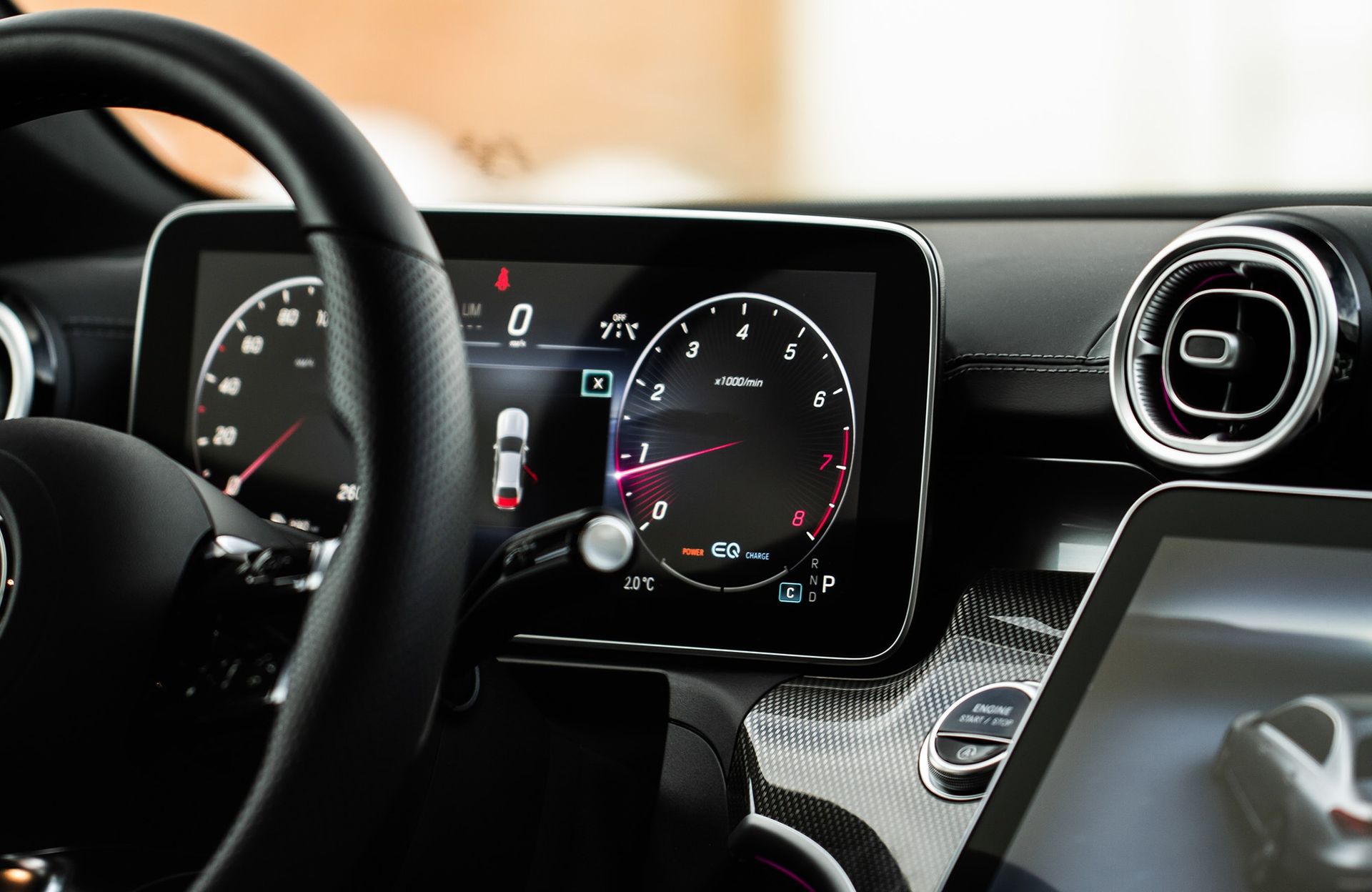 A close-up view of a car’s digital dashboard and steering wheel, featuring glowing gauges and a center touchscreen.