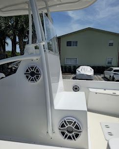 Boat deck seats with speakers overlooking a parked car and pale green building on a sunny day