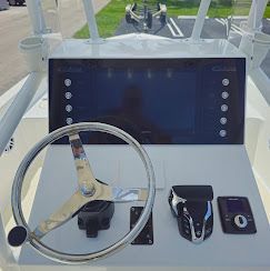 Boat helm with steering wheel, large display screen, and control switches on a white console