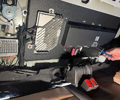 Person using a screwdriver on electronic equipment inside an open machine compartment