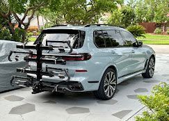 Silver SUV with a rear-mounted bike rack parked in a driveway, surrounded by trees and greenery