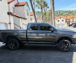 Black pickup truck parked beside apartment buildings with palm trees in the background