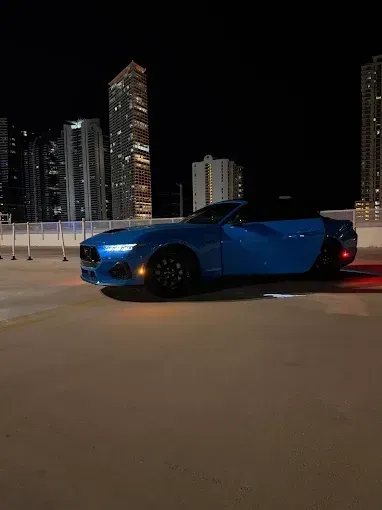 Blue sports car parked at night on a city street with illuminated skyscrapers in the background