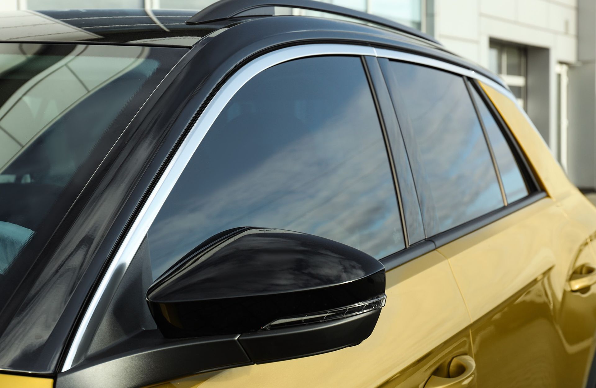 A golden SUV with black window trim, black side mirrors, and a black roof rack parked outdoors.