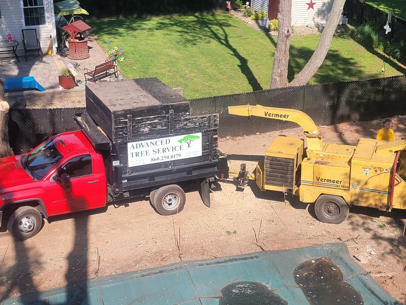 Red truck and wood chipper processing tree debris in a yard.
