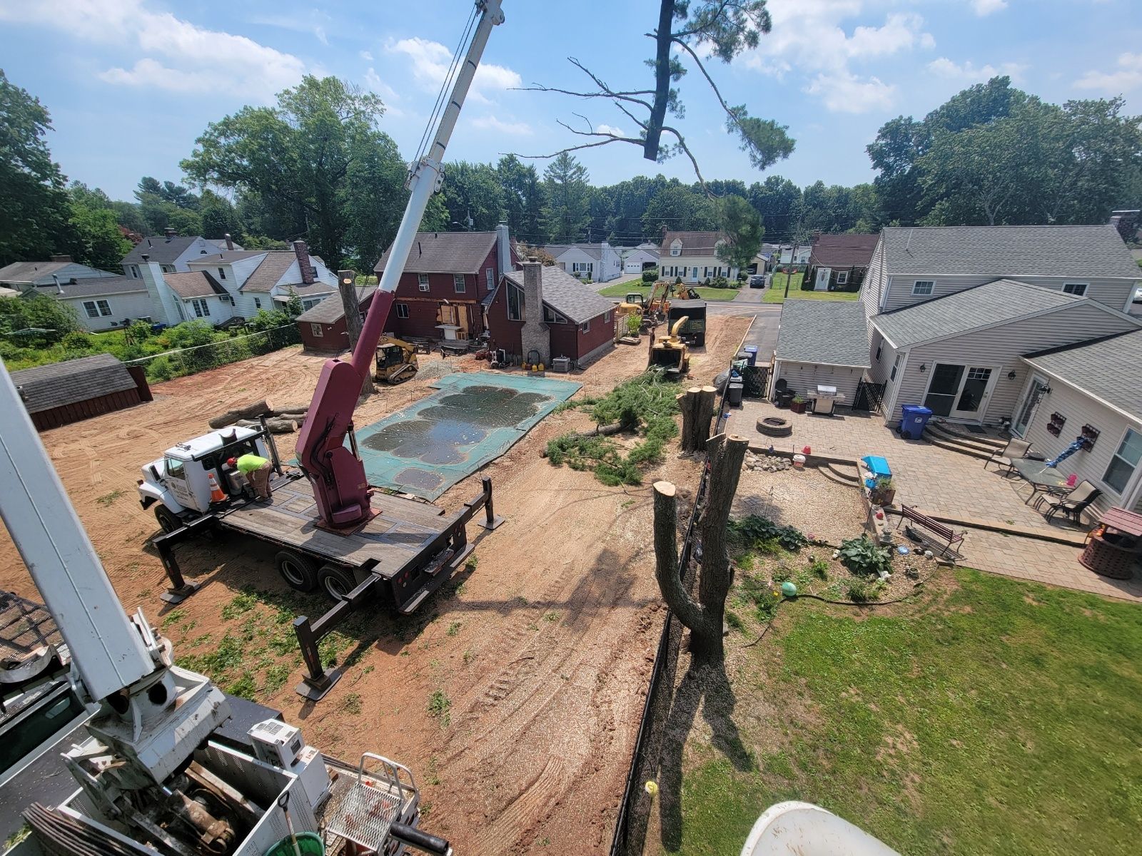 Tree removal operation; cherry picker over debris-strewn yard with houses and equipment.