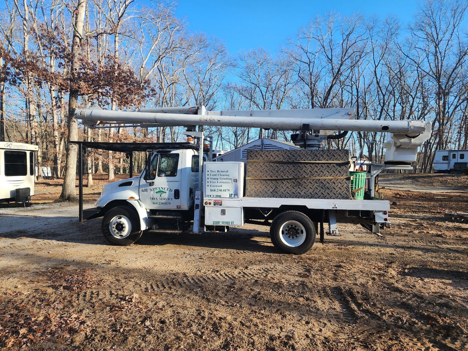 White utility truck with extended boom parked outdoors, trees in background.