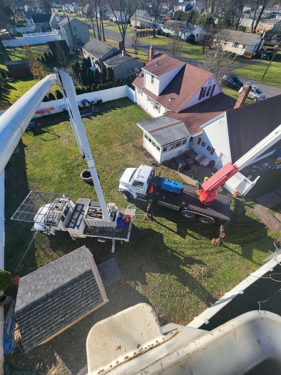 Aerial view of a truck with a crane working near a white house with a brown roof and a small building.