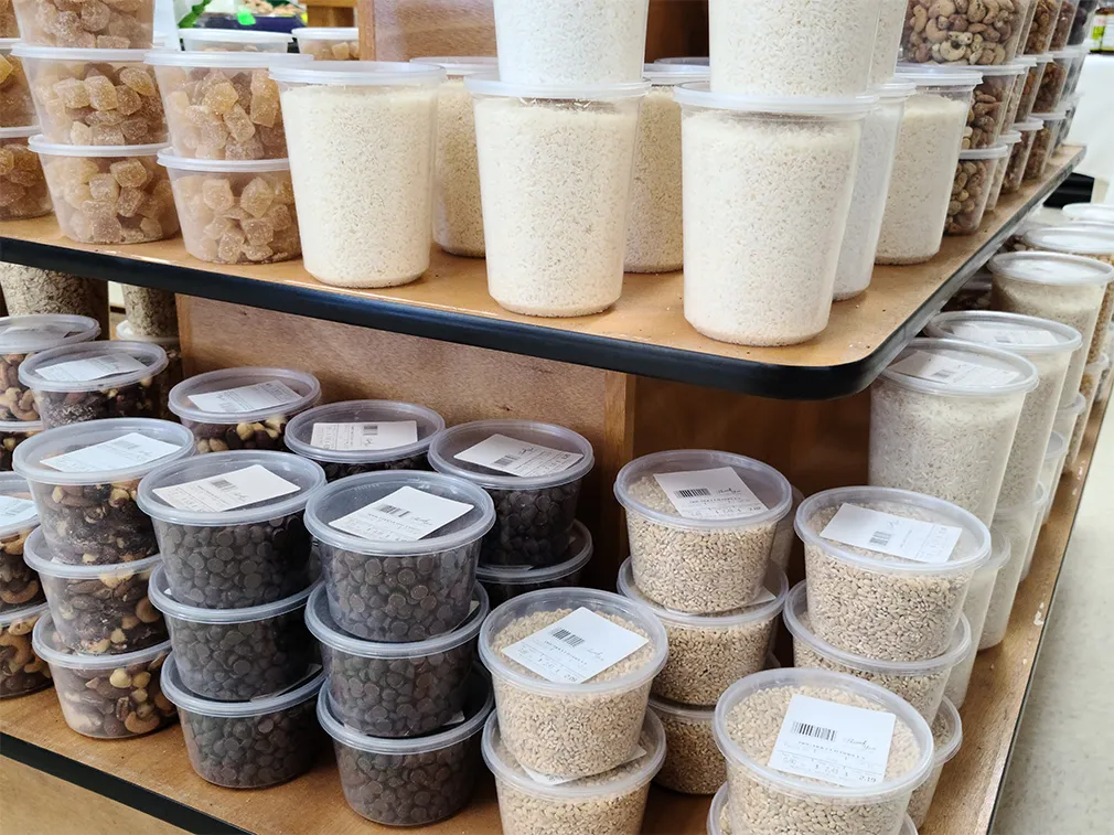 Shelves stocked with clear plastic containers of various grains and nuts in a store setting.