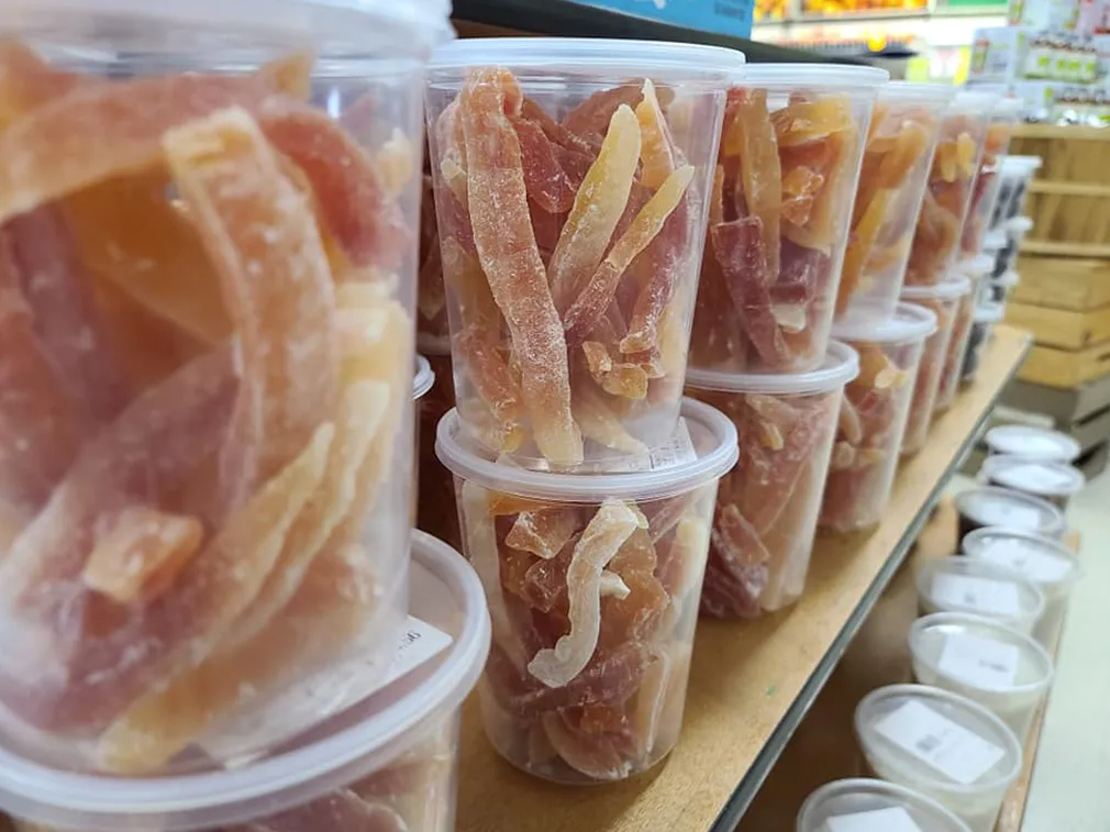 Rows of clear plastic containers filled with dried papaya strips on a store shelf.