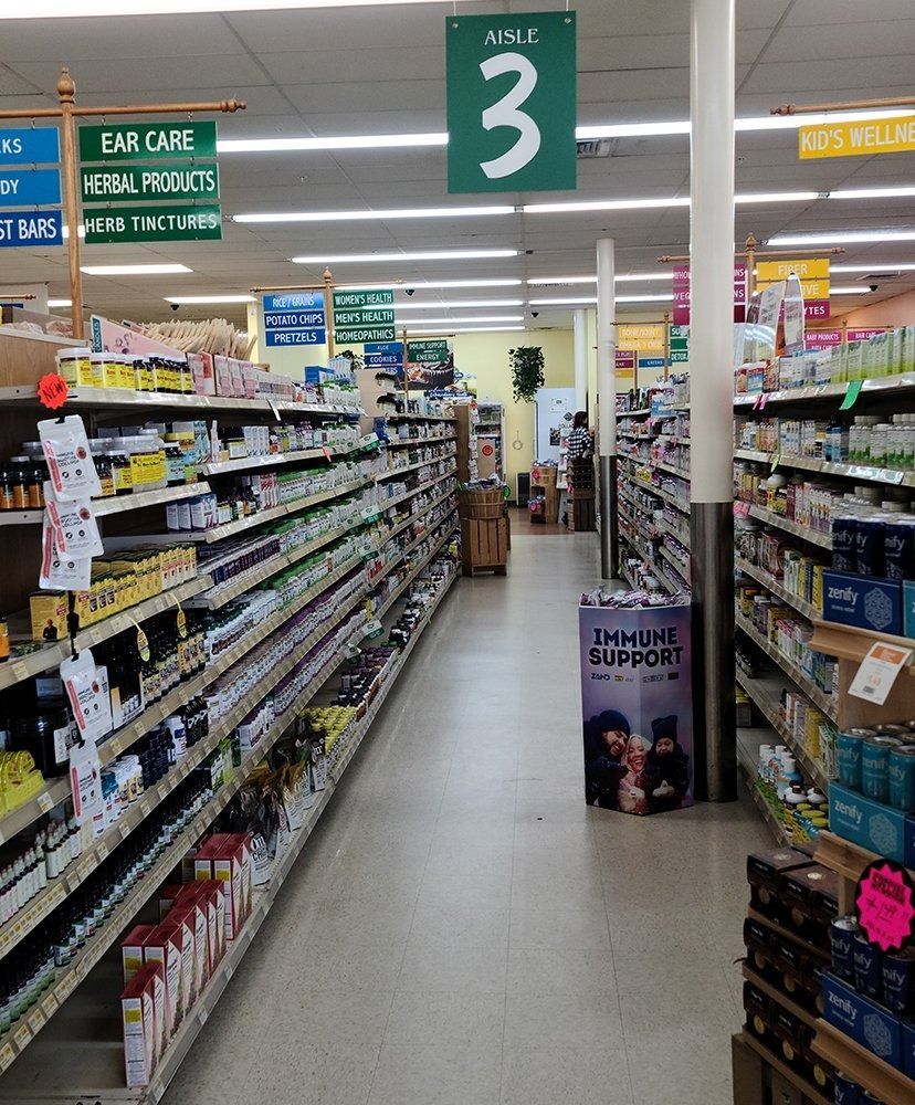 Grocery store aisle with shelves of products, green signs, and a 