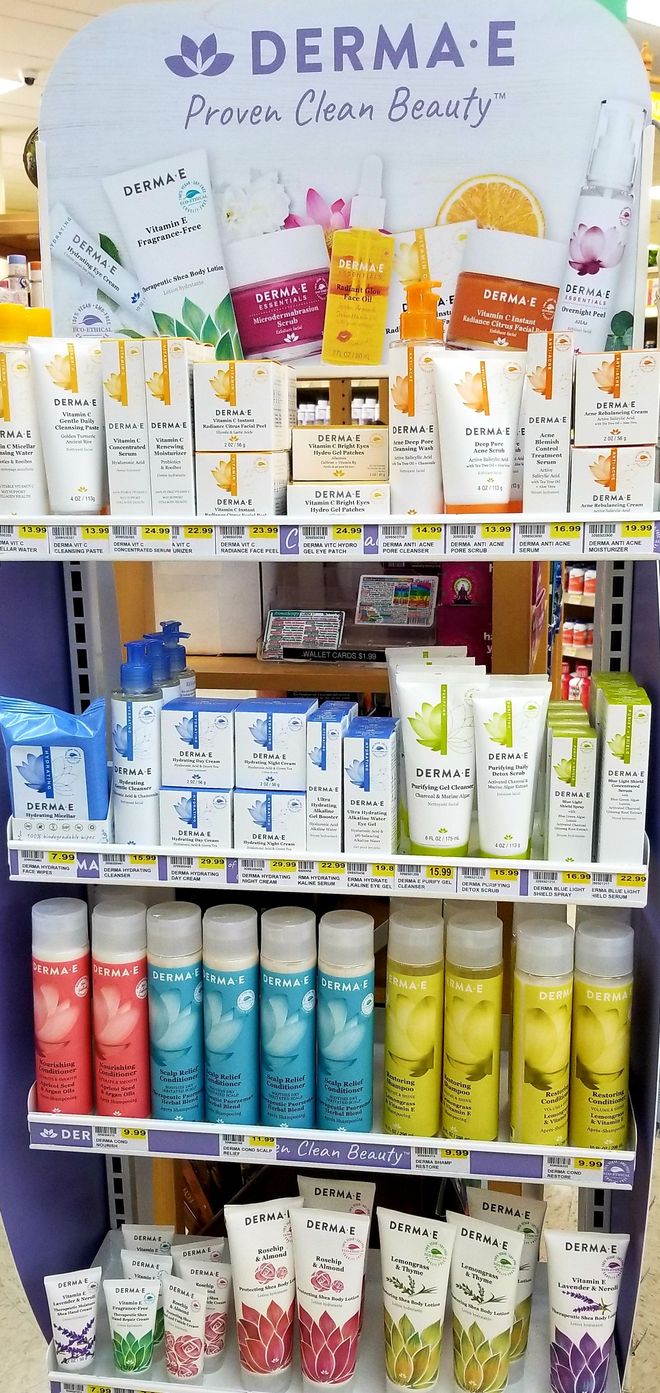 A display of Derma E beauty products on shelves in a store. Products are in various colors and packaging.