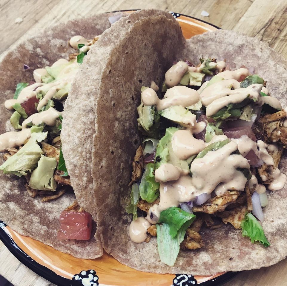 Two tacos on a plate, filled with lettuce, avocado, and sauce; close-up view.