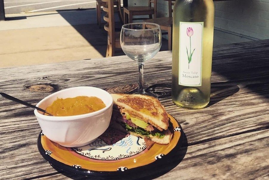 Soup, sandwich, and wine bottle on a rustic table, outside.