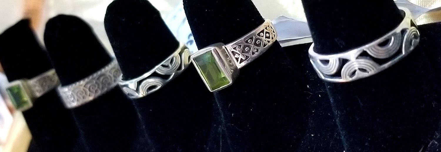 Close-up of several silver rings on black ring display. Some have stone accents or openwork designs.