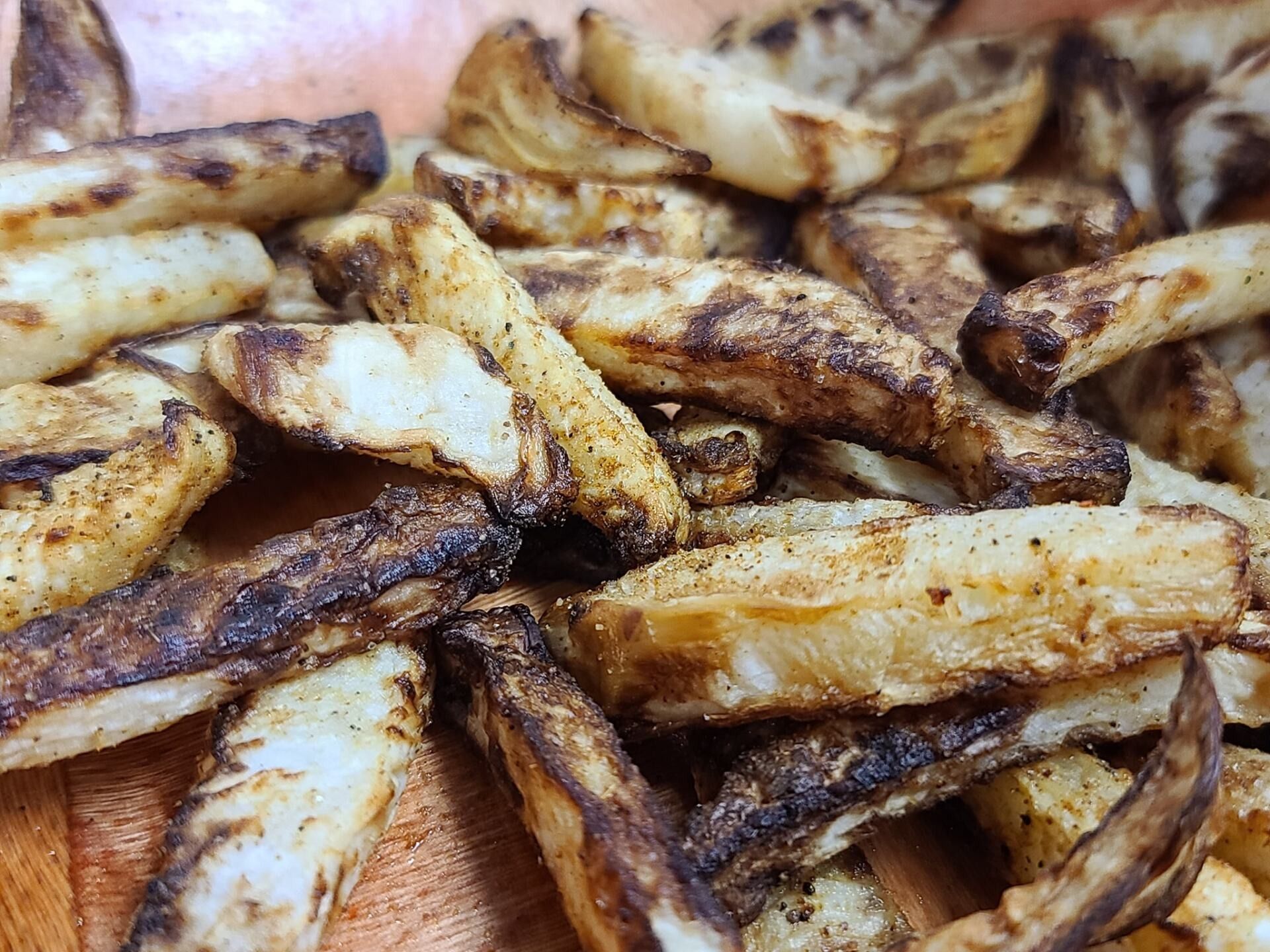 Crispy, seasoned potato wedges piled on a wooden surface. Browned edges, white insides.