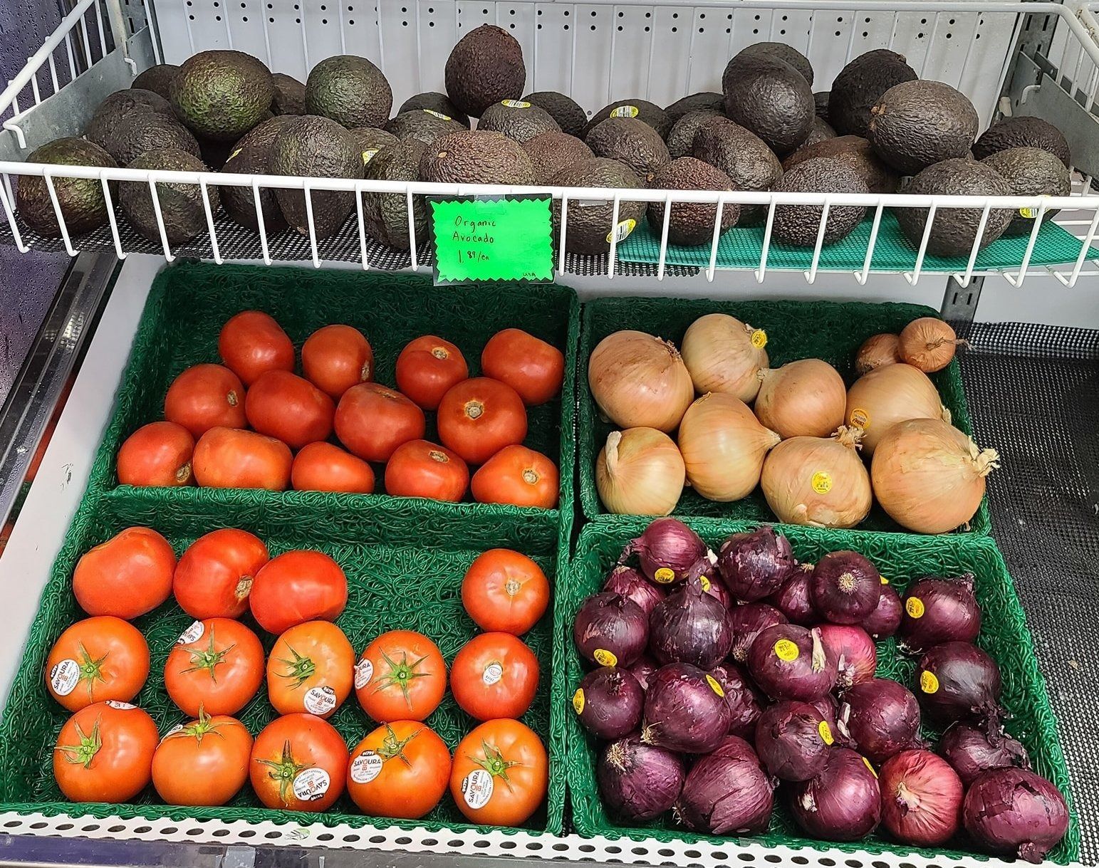 Produce shelf: avocados, tomatoes, potatoes, and red onions.