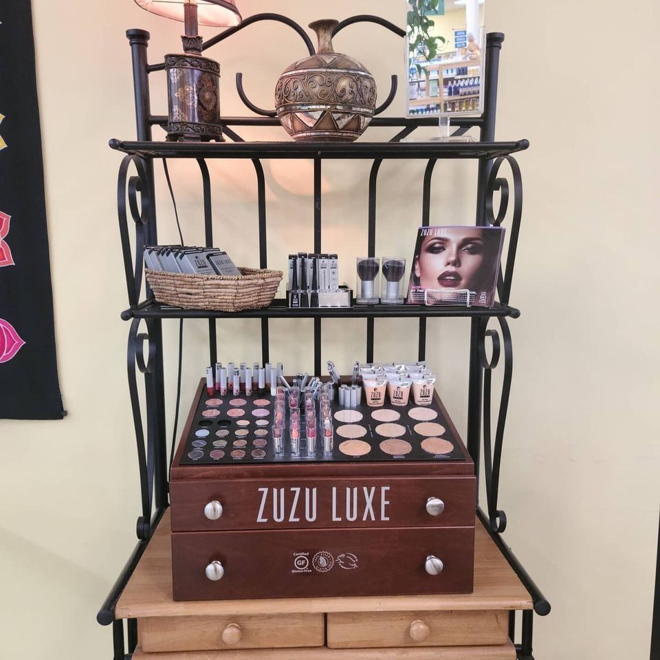 Makeup display stand with Zuzu Luxe products, plus decorative objects, against a cream wall.