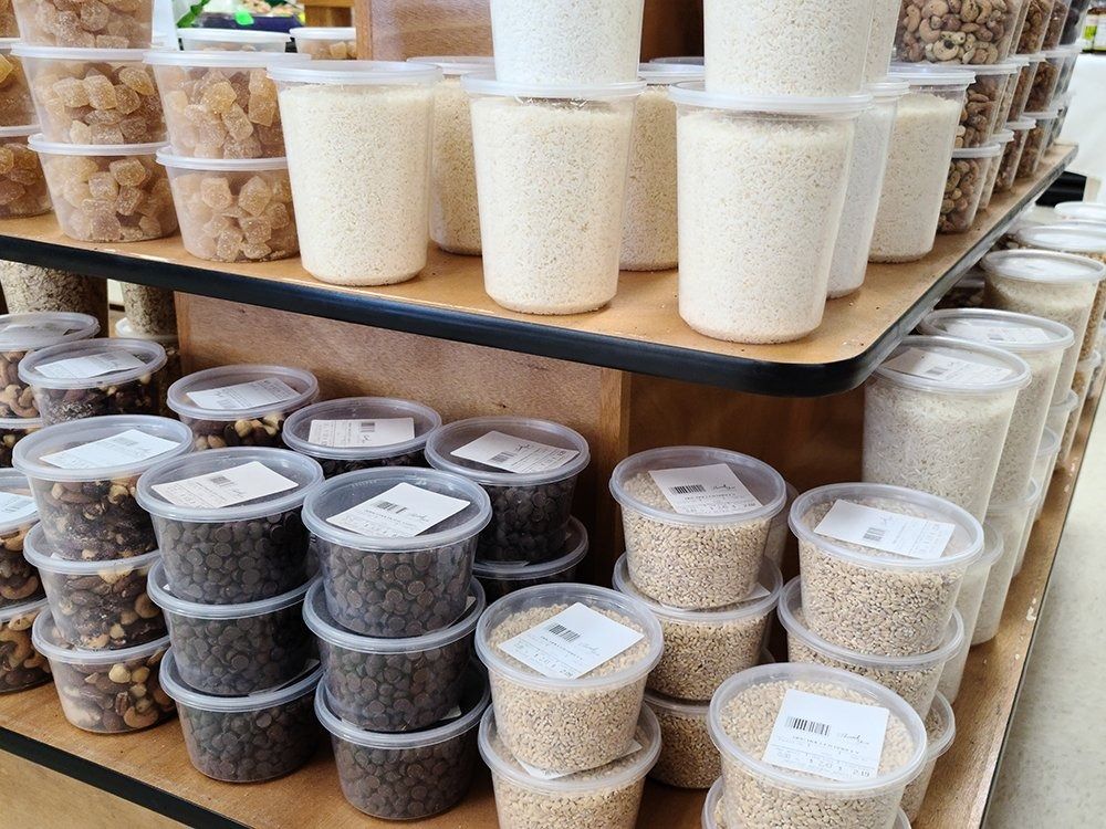 Shelves of plastic containers filled with various grains and nuts for bulk food shopping.