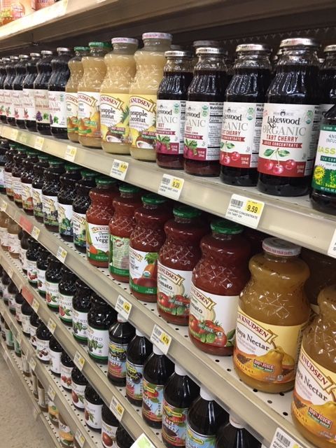 Bottles of juice on shelves in a grocery store. Varieties include tomato, cranberry, and orange, with various label colors.