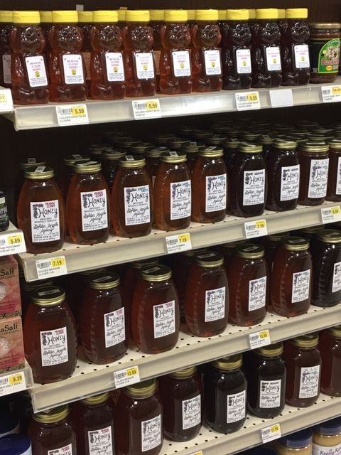Honey jars in various sizes and colors displayed on grocery store shelves.