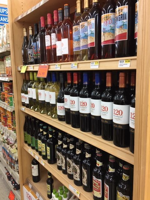 Shelves of wine bottles in a store, various colors and labels. Wooden shelves and beige walls.
