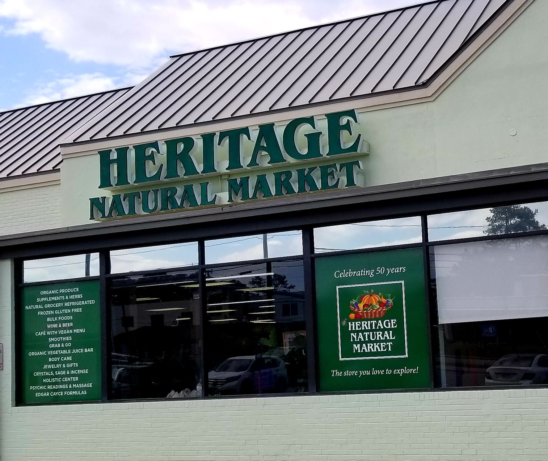 Heritage Natural Market storefront with green sign, glass windows, and parked cars.