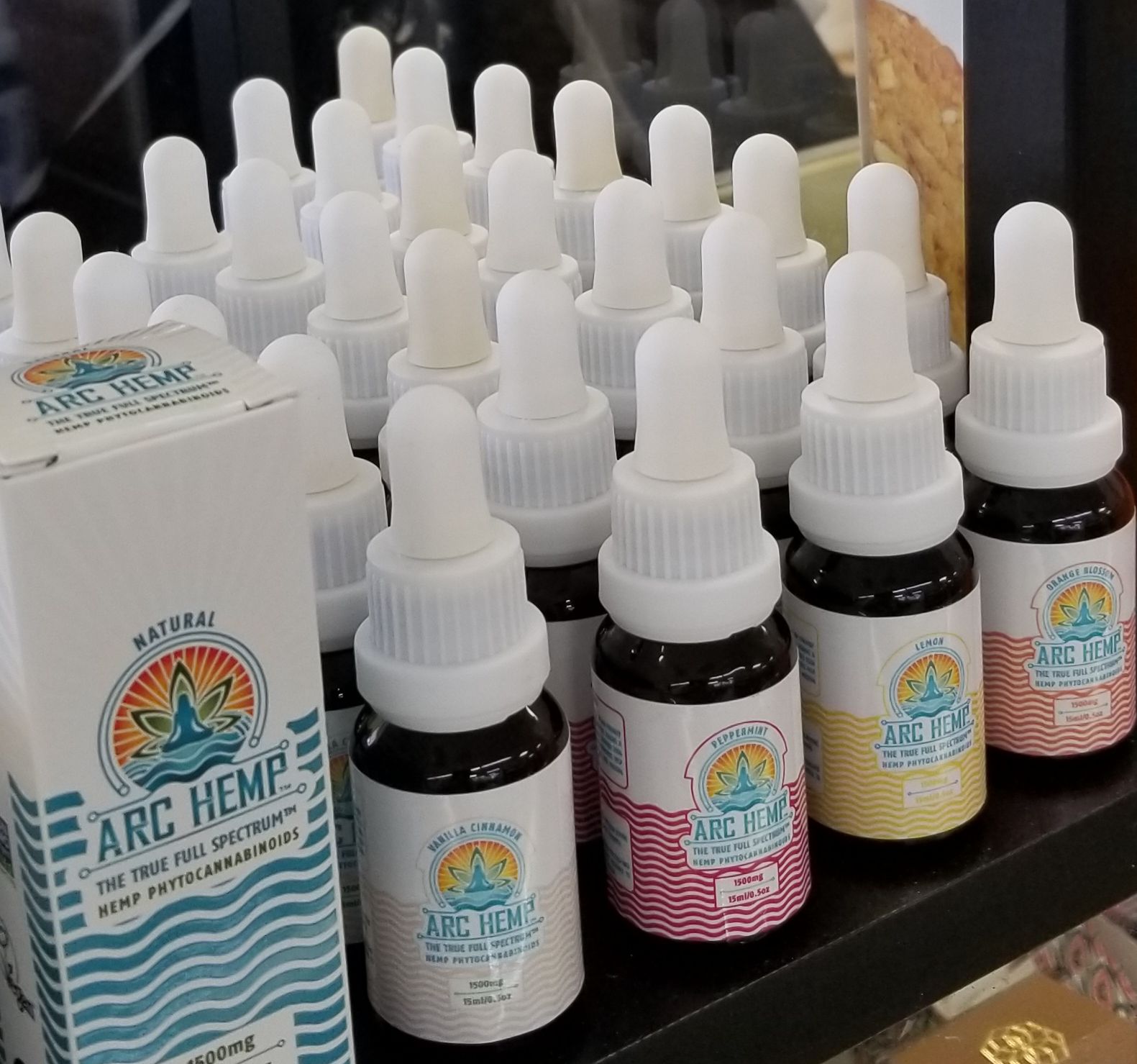Bottles of Arc Hemp oil in various colors, with droppers, arranged on a shelf next to a box.