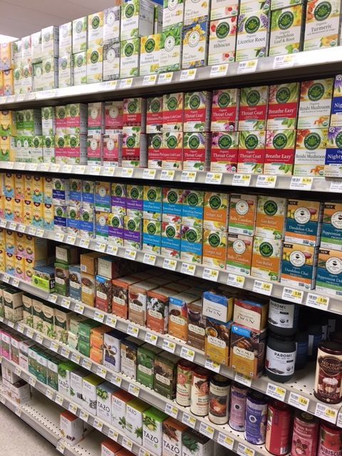Shelves stocked with various herbal tea boxes in a grocery store. Bright colors, organized displays.