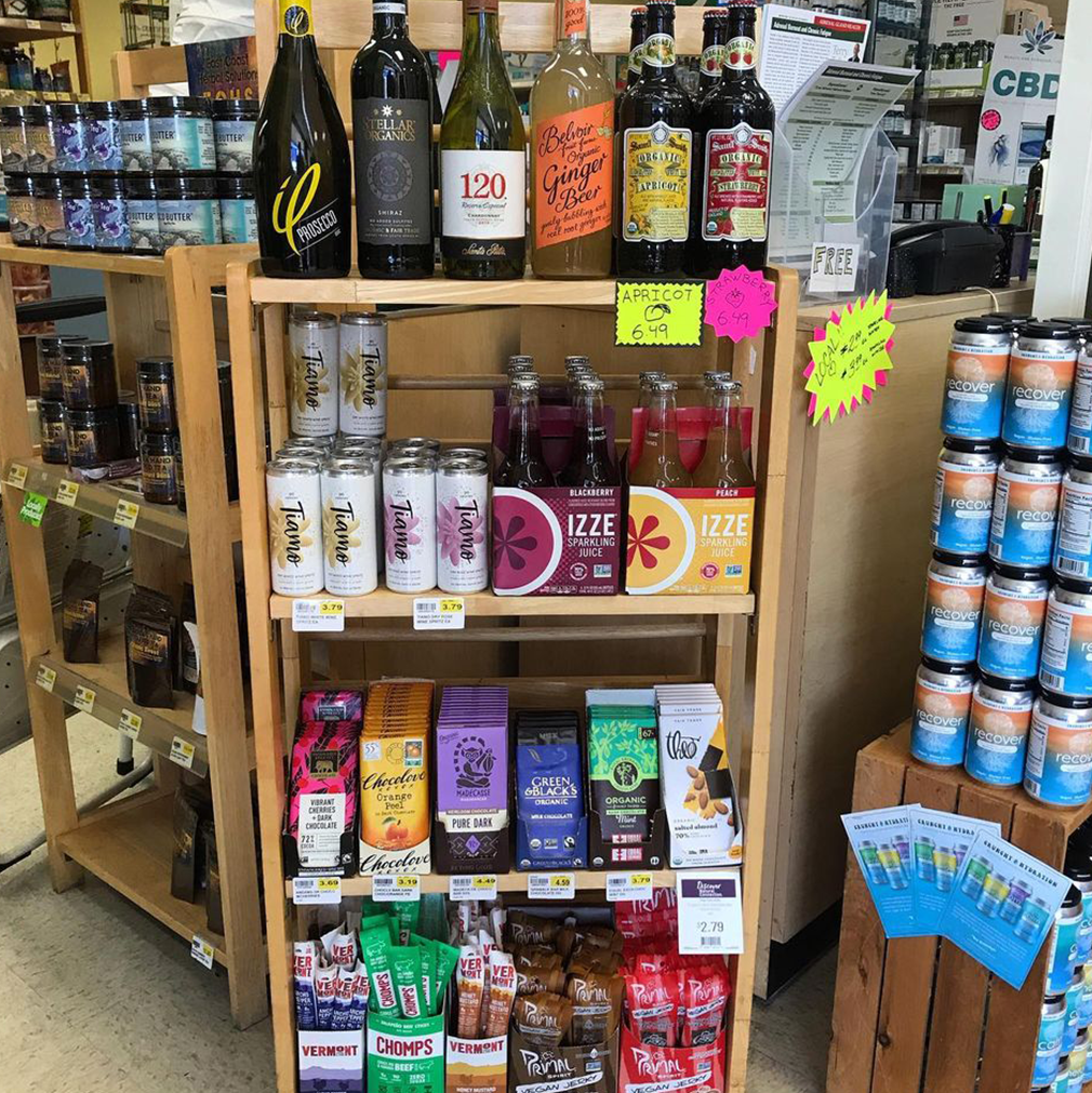 Wooden shelf stocked with various beverages: wine, soda, beer, coffee, and snacks in a store.