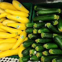 Yellow squash and green zucchini arranged in bins at a produce market.