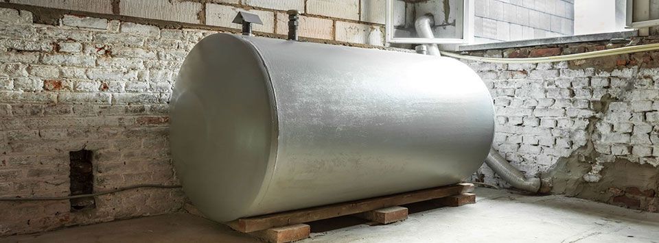 An oil tank rests on wooden beams in a basement. Brick walls surround it.