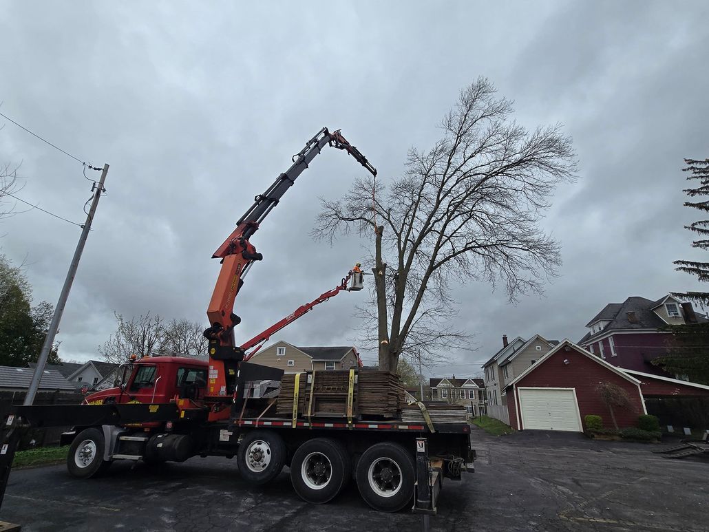 Crane truck loading lumber on a flatbed in a residential street under cloudy skies