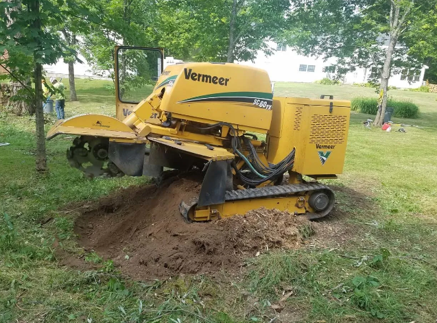 Yellow farm tractor digging soil in a grassy yard near trees